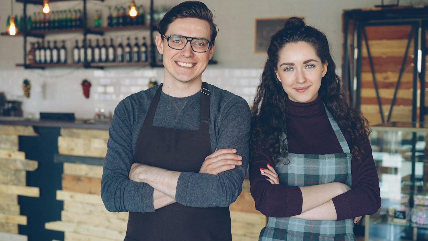 Two café owners in aprons standing behind their counter